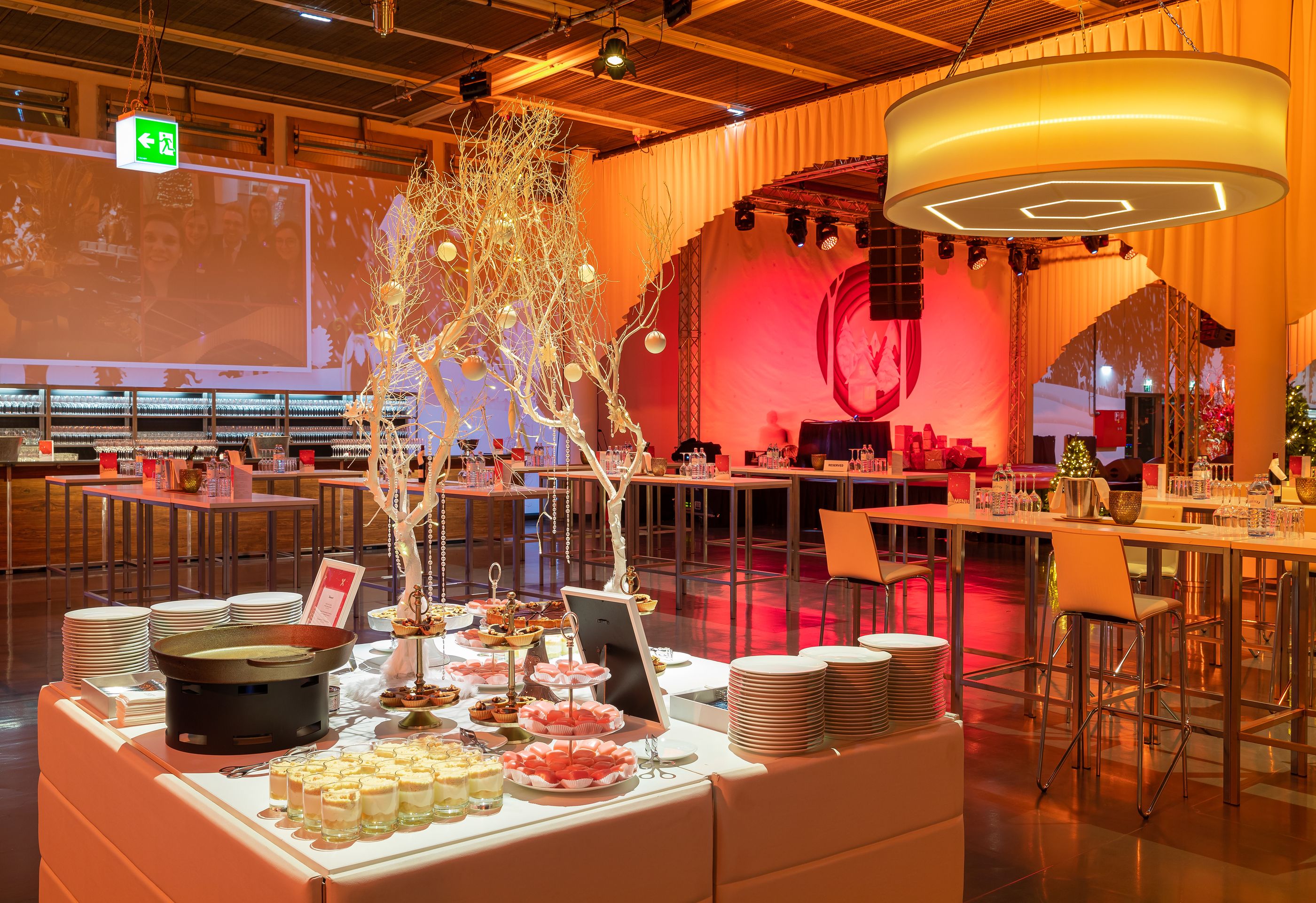 Foto: Eine Halle mit einem Buffettisch, gedeckten Tischen, Lampen und Wandprojektion