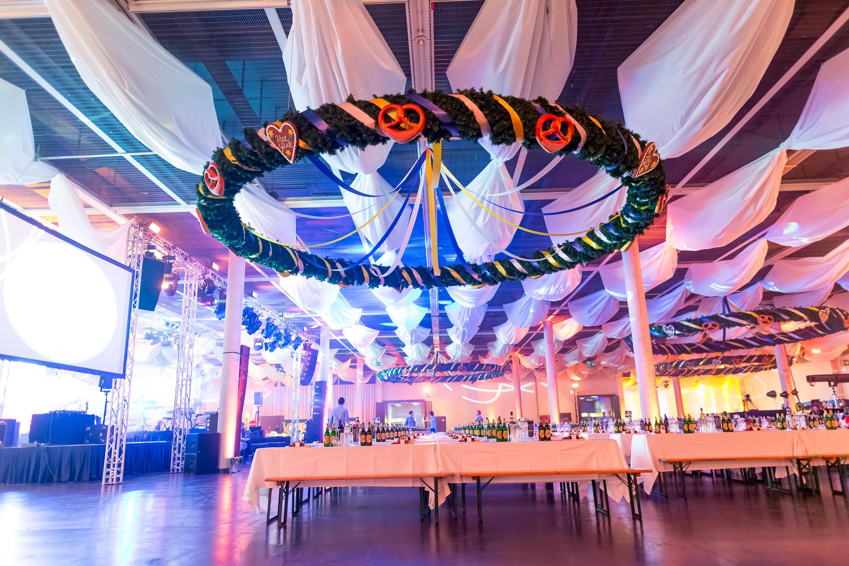 Foto: Oktoberfest-Kranz in einer Halle mit Biertischen und weißer Decken-Deko