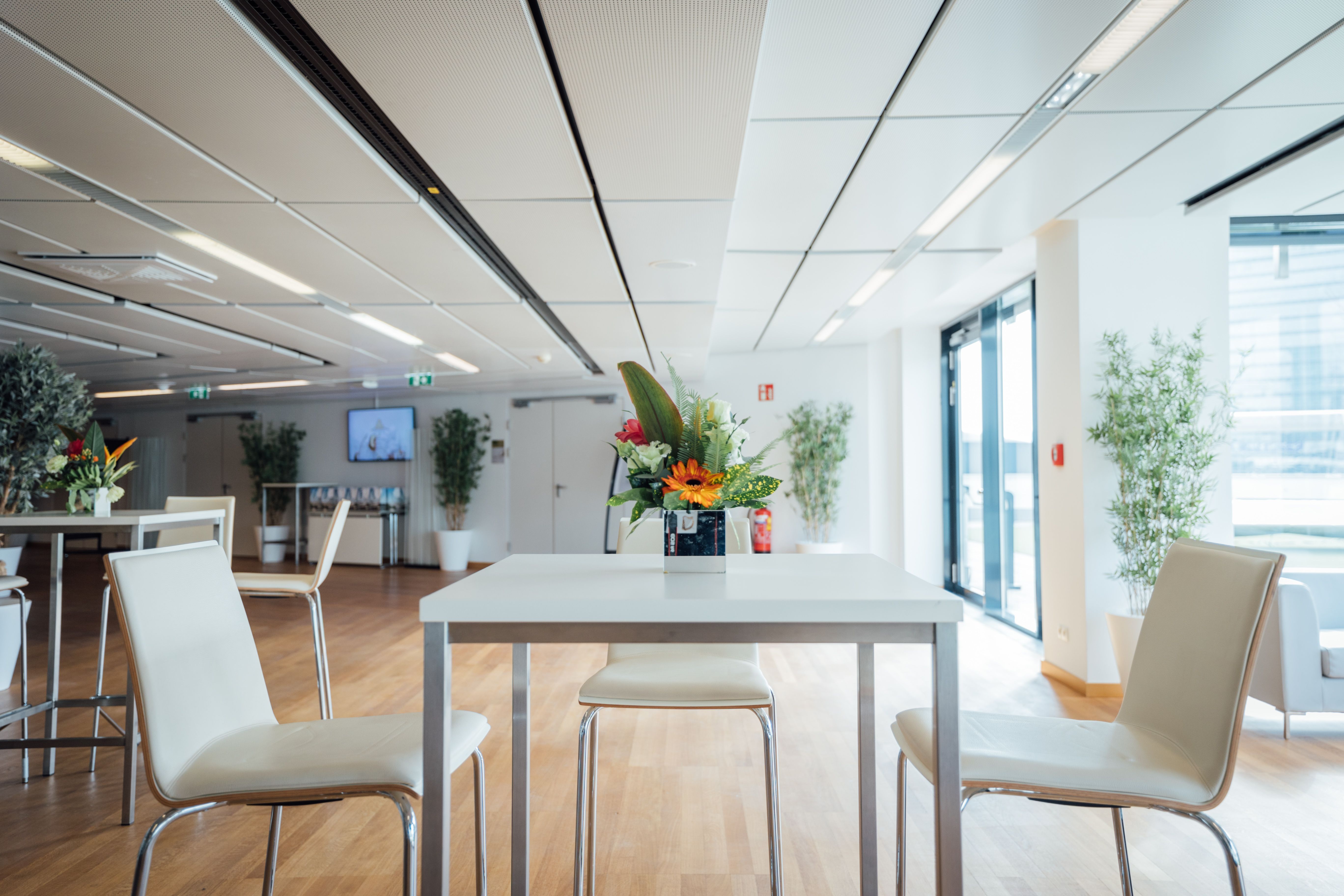 Foto: heller Raum mit Holzboden und Fenstern, Stuehlen, Tisch, Blumen