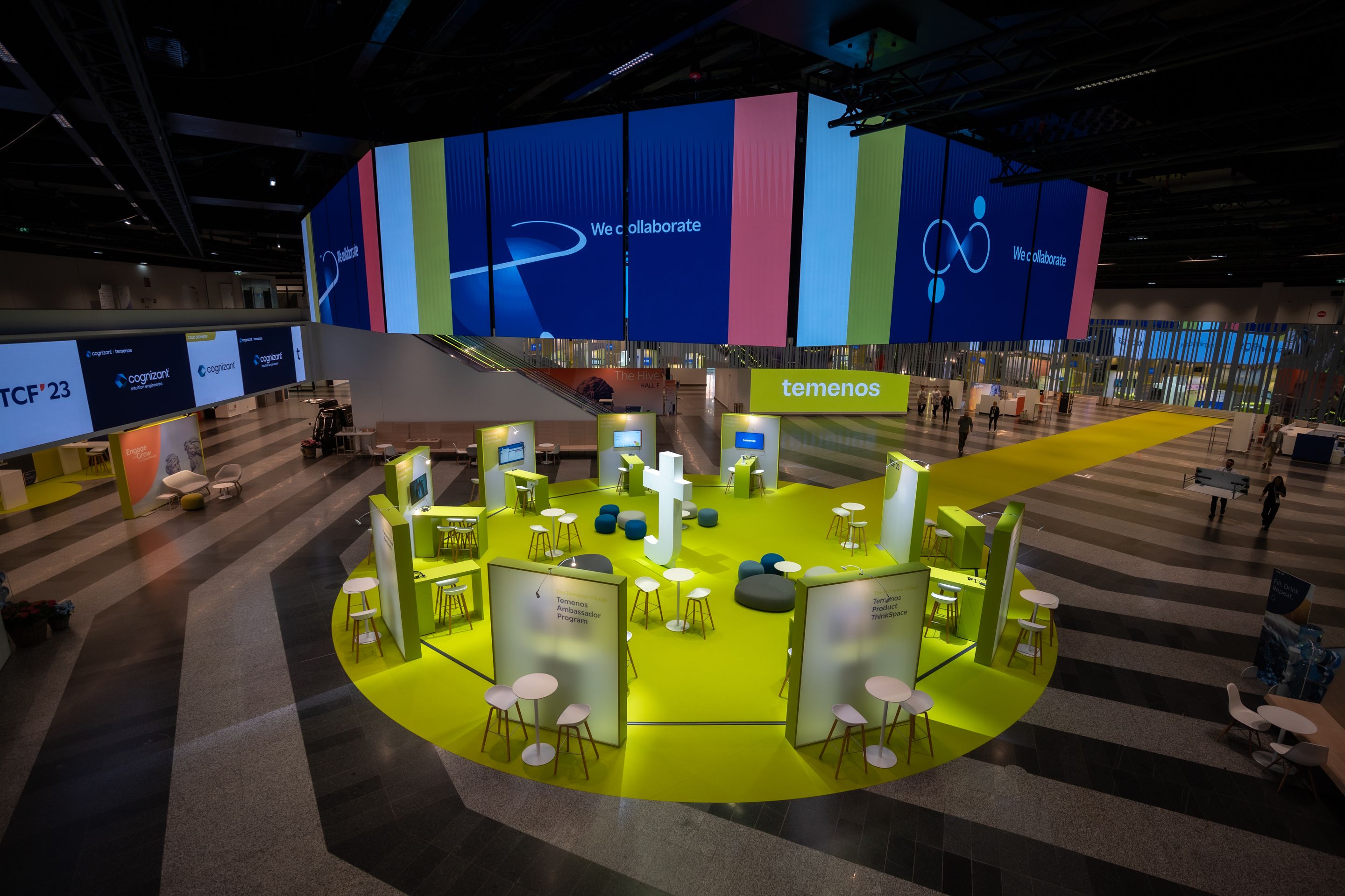 Foto: eine Halle mit bunt beleuchteten Werbe-Flaechen, Sitzgruppen und gelben Teppich