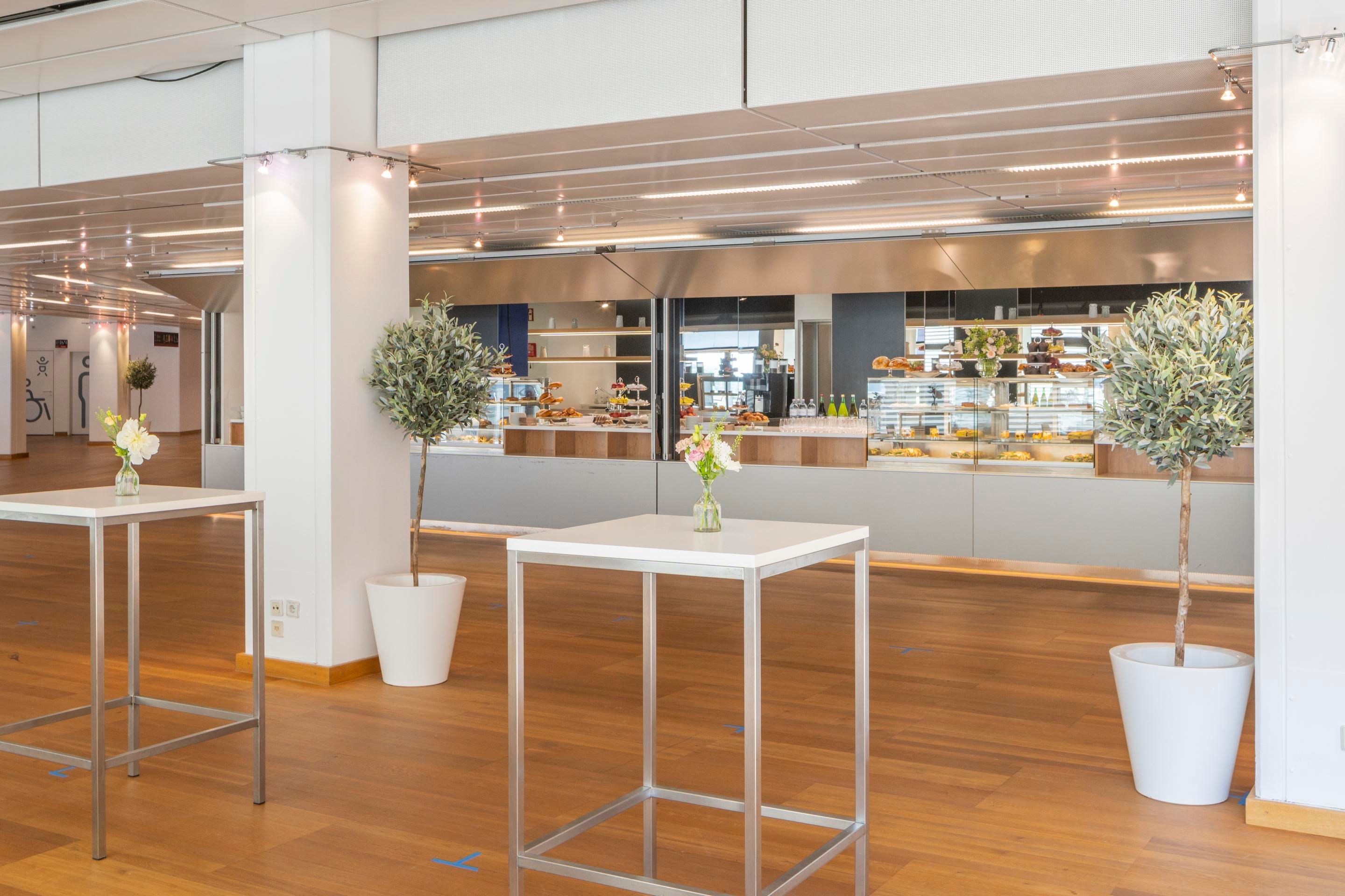 Foto: Raum mit Holzboden und hellen Saeulen, Stehtischen und einem Café