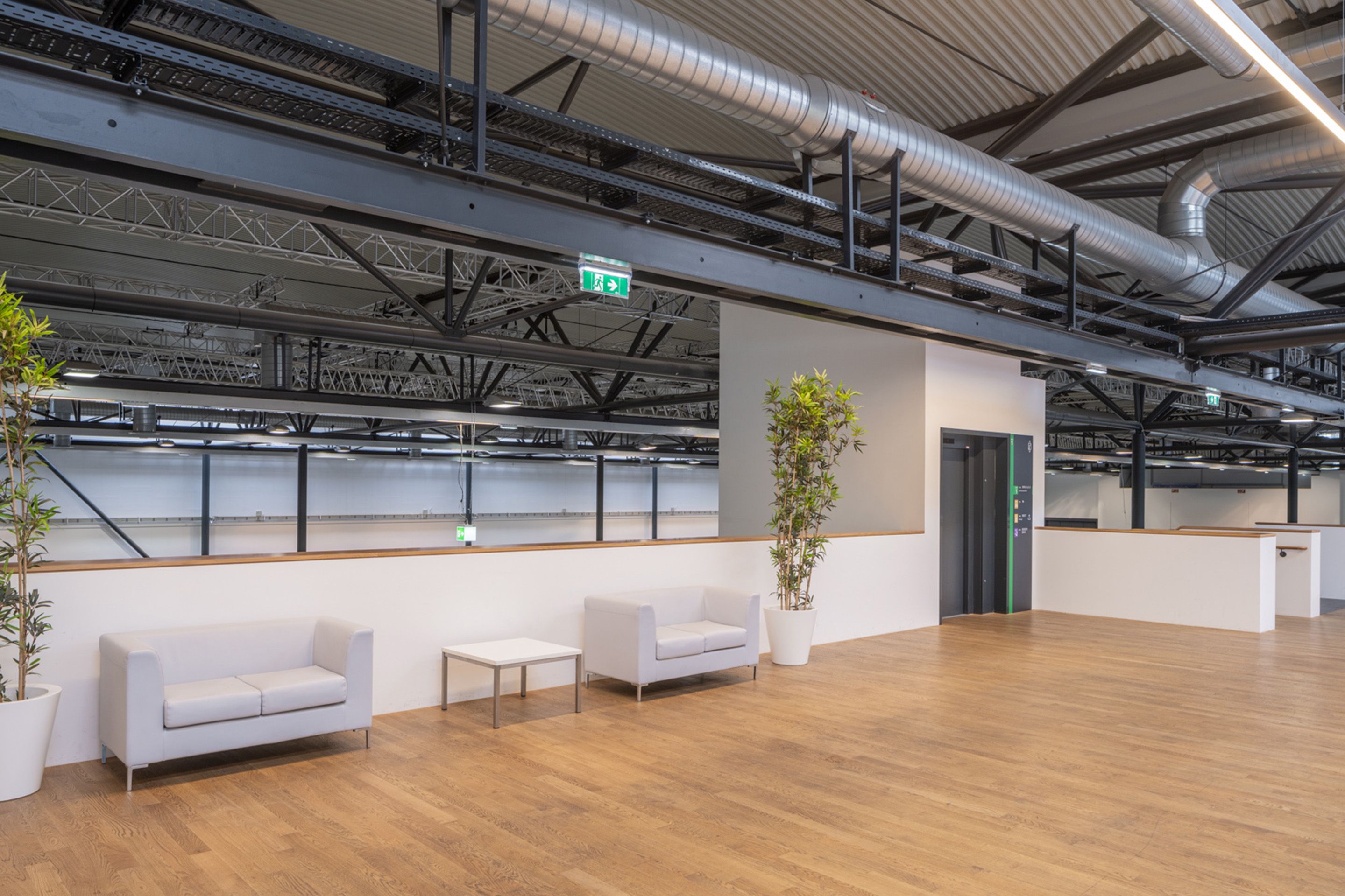 Foto: Bereich mit Holzboden, hellen Moebeln und einem Lift in einer Halle