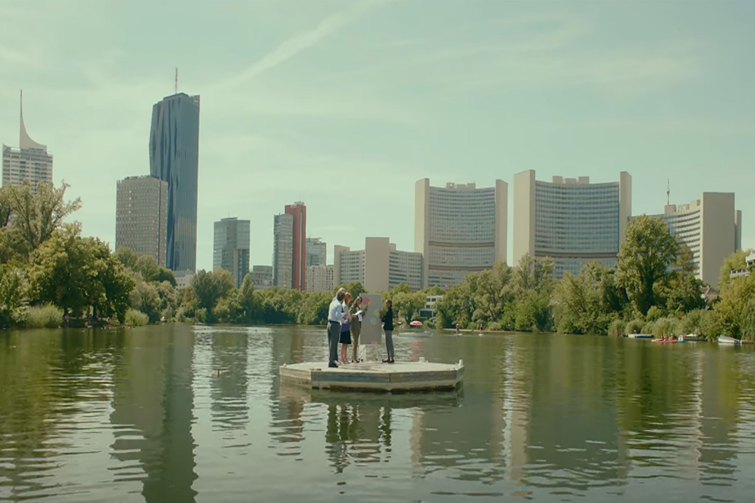 Foto: Menschen stehen auf deiner Plattform in einem See mit Hochhaeuern im Hintergrund