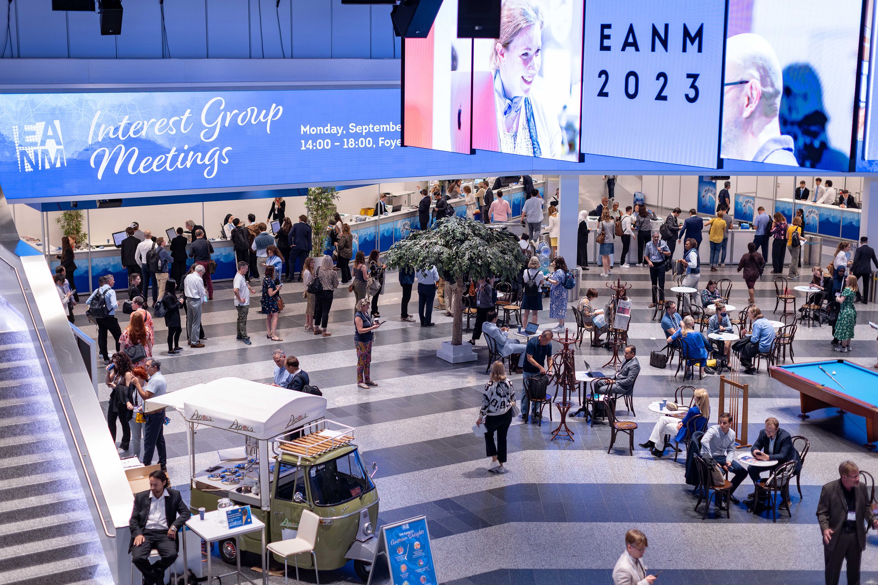 Foto: Halle mit vielen Menschen, hell beleuchteten LED Waenden, Baeumen und einer Rolltreppe