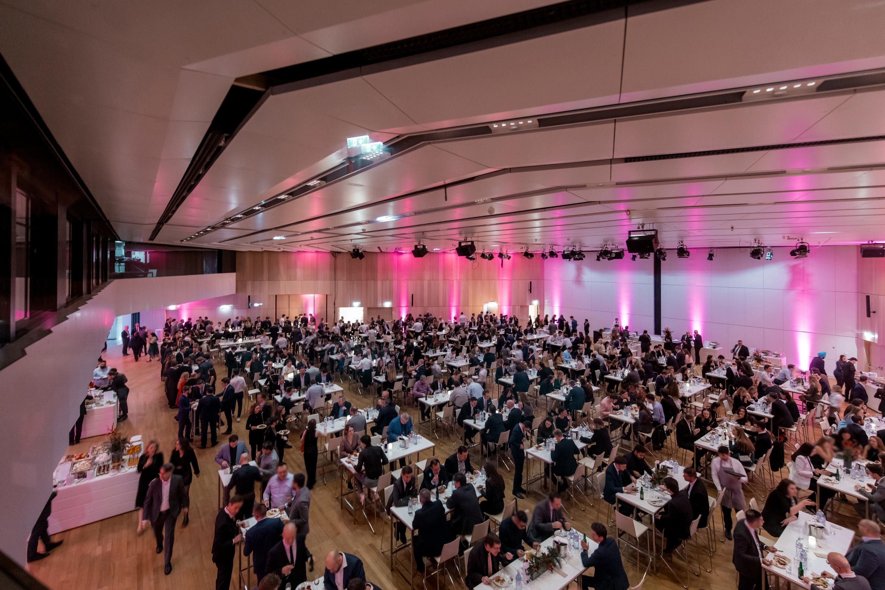 Foto: Esstische mit Menschen in einer pink beleuchteten Halle