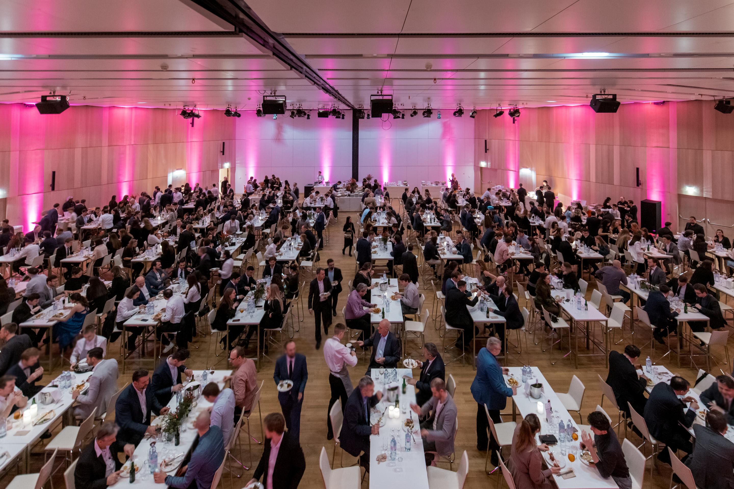 Foto: Esstische mit Menschen in einer pink beleuchteten Halle