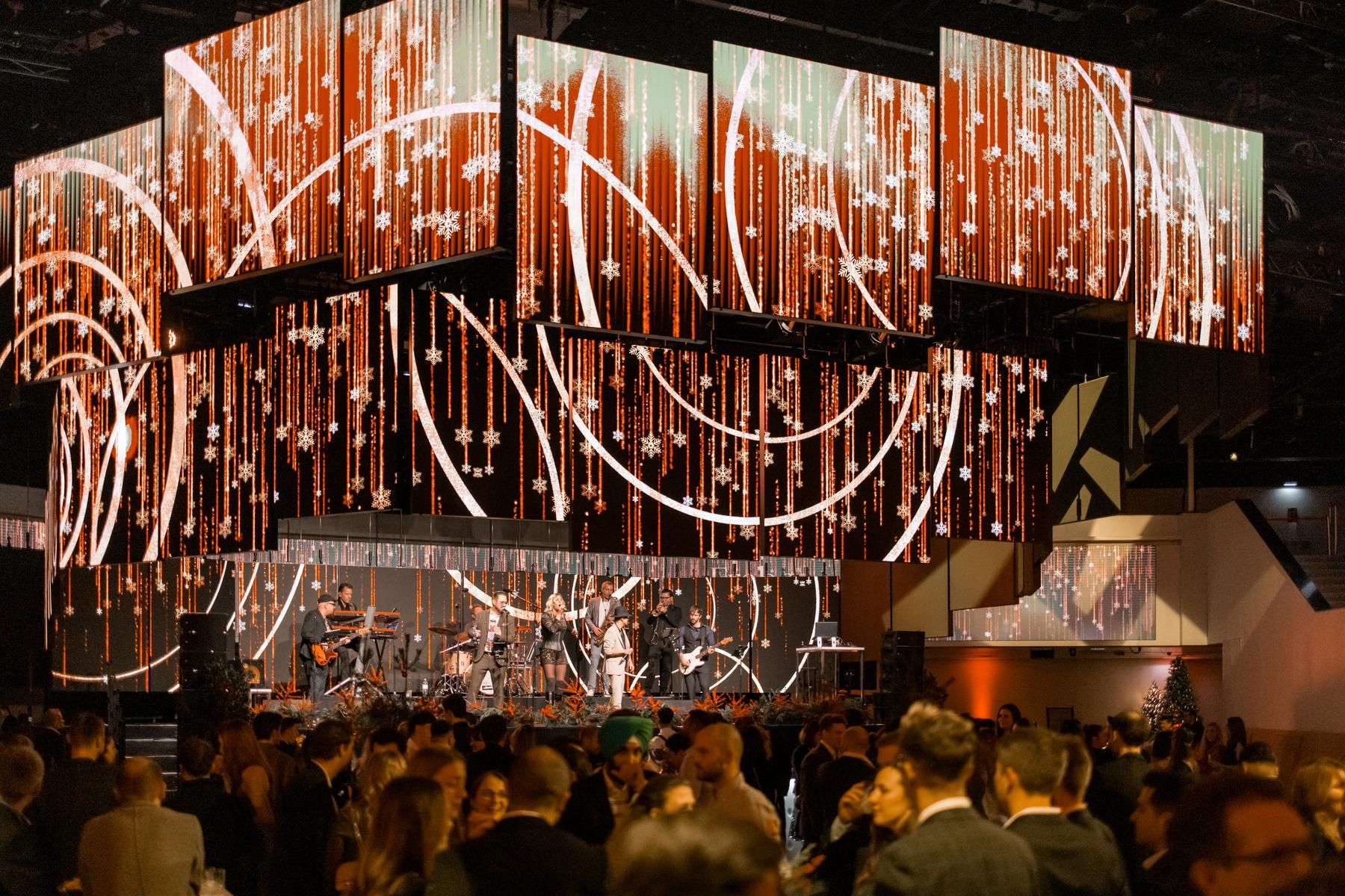 Foto: weihnachtlich beleuchtete LED-Paneele mit einer Band und Buehne in einer Halle mit Menschen