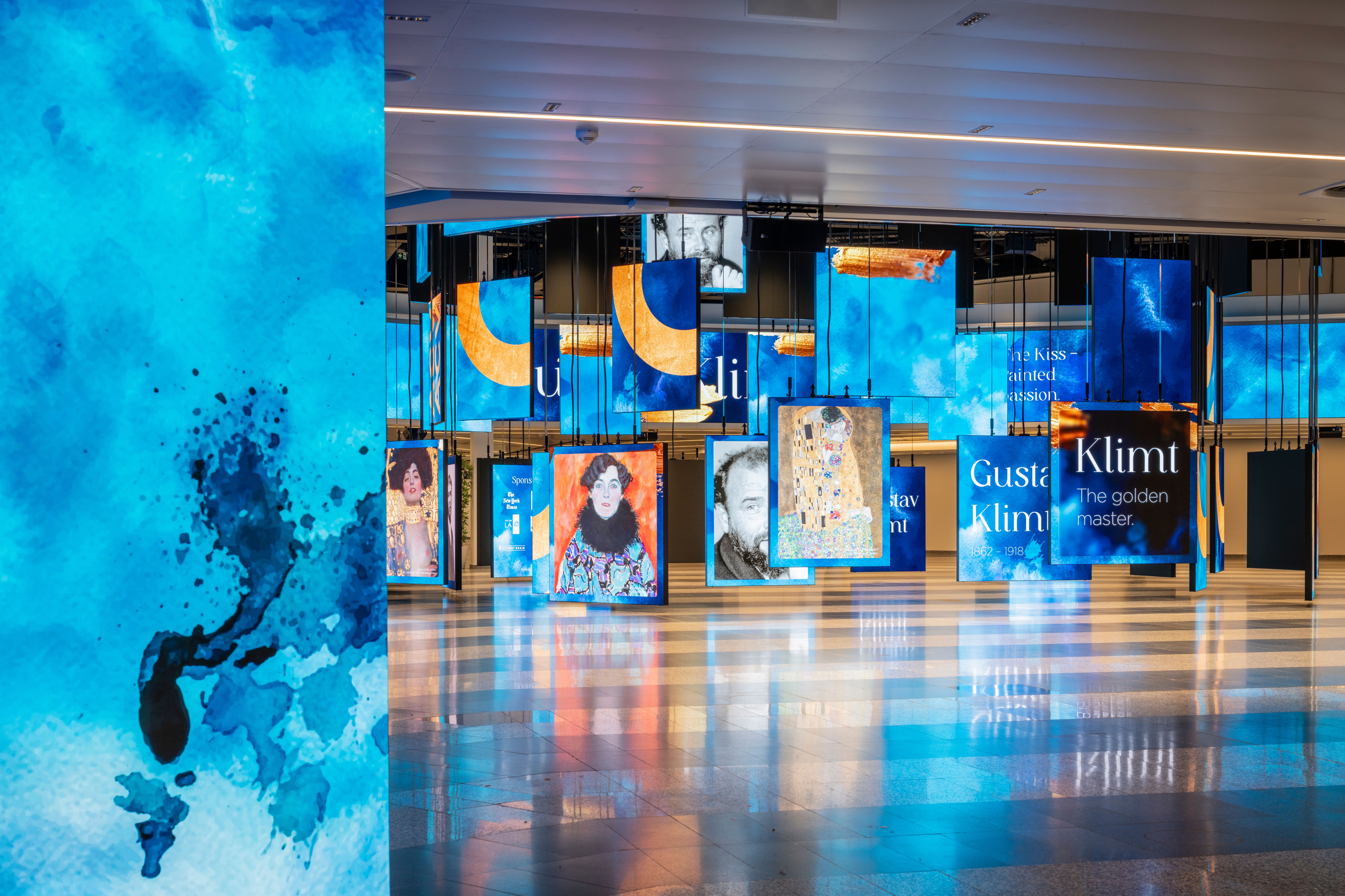 Foto: blaue beleuchtete Paneele mit Klimt Bildern in einer Halle