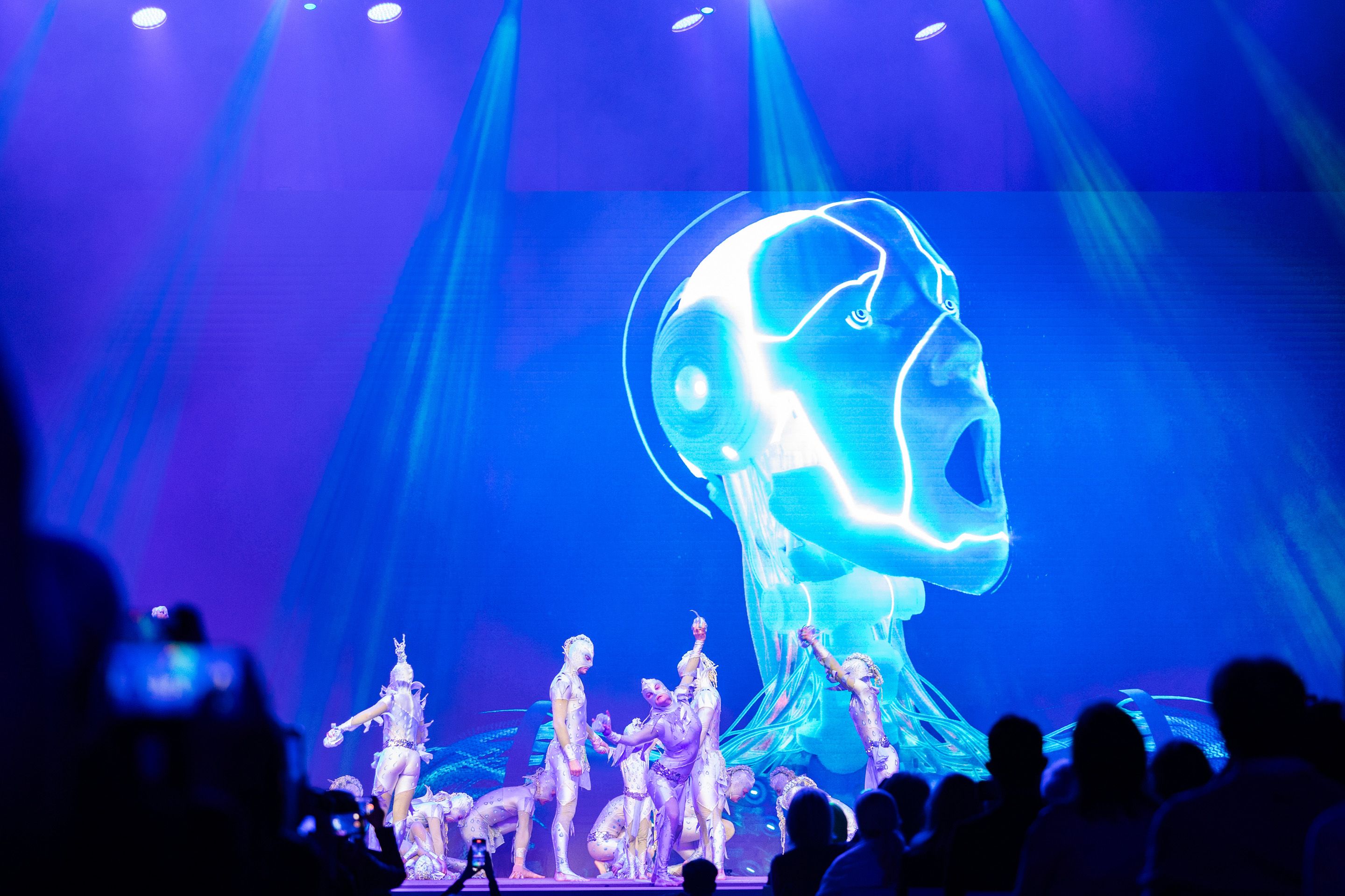 Foto: Akrobatik Taenzer in Kostuemen bei ihrer Auffuehrung. Im Hintergrund ein Roboterkopf