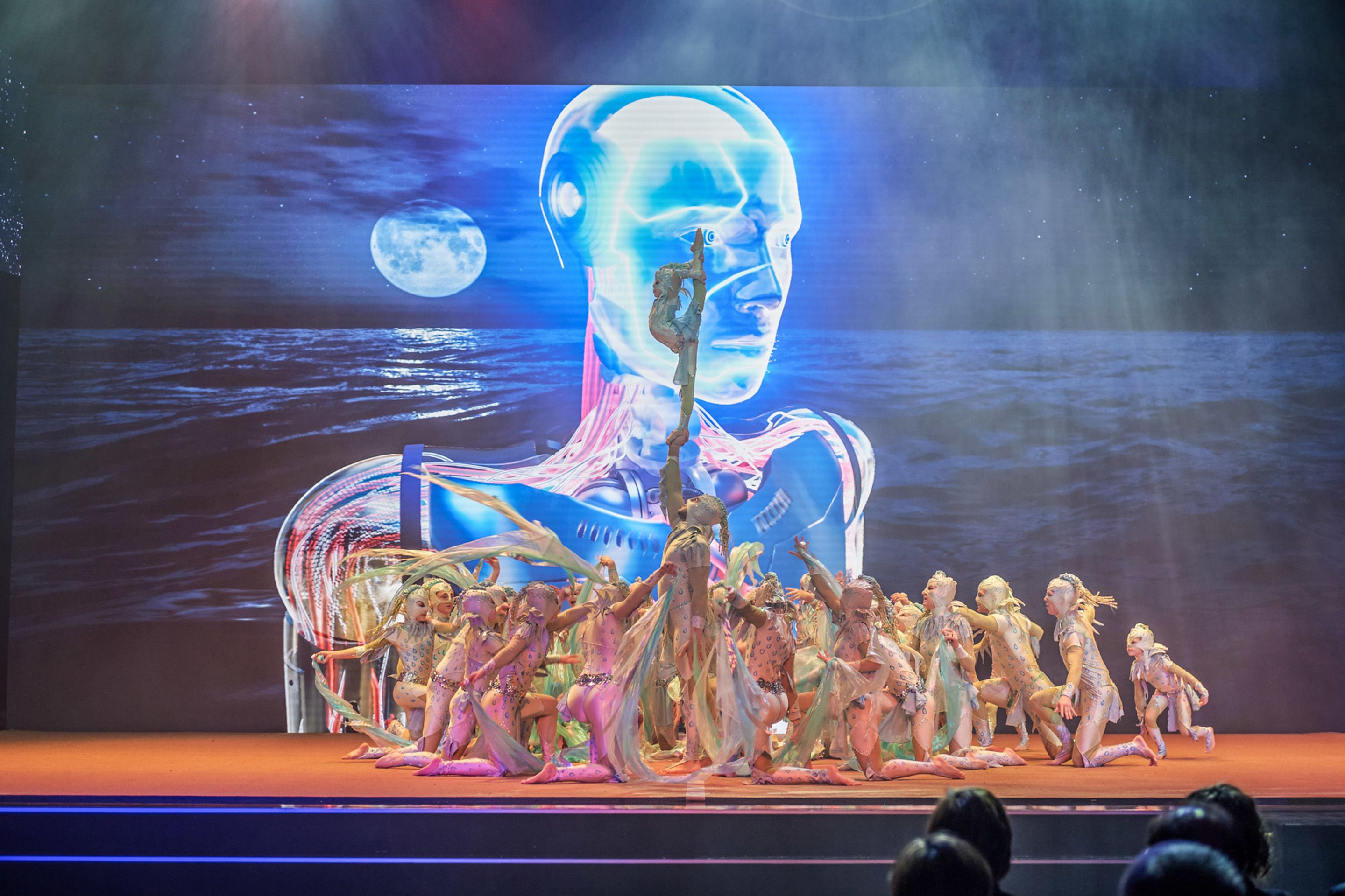 Foto: Akrobatik Taenzer in Kostuemen bei ihrer Auffuehrung. Im Hintergrund ein Roboterkopf