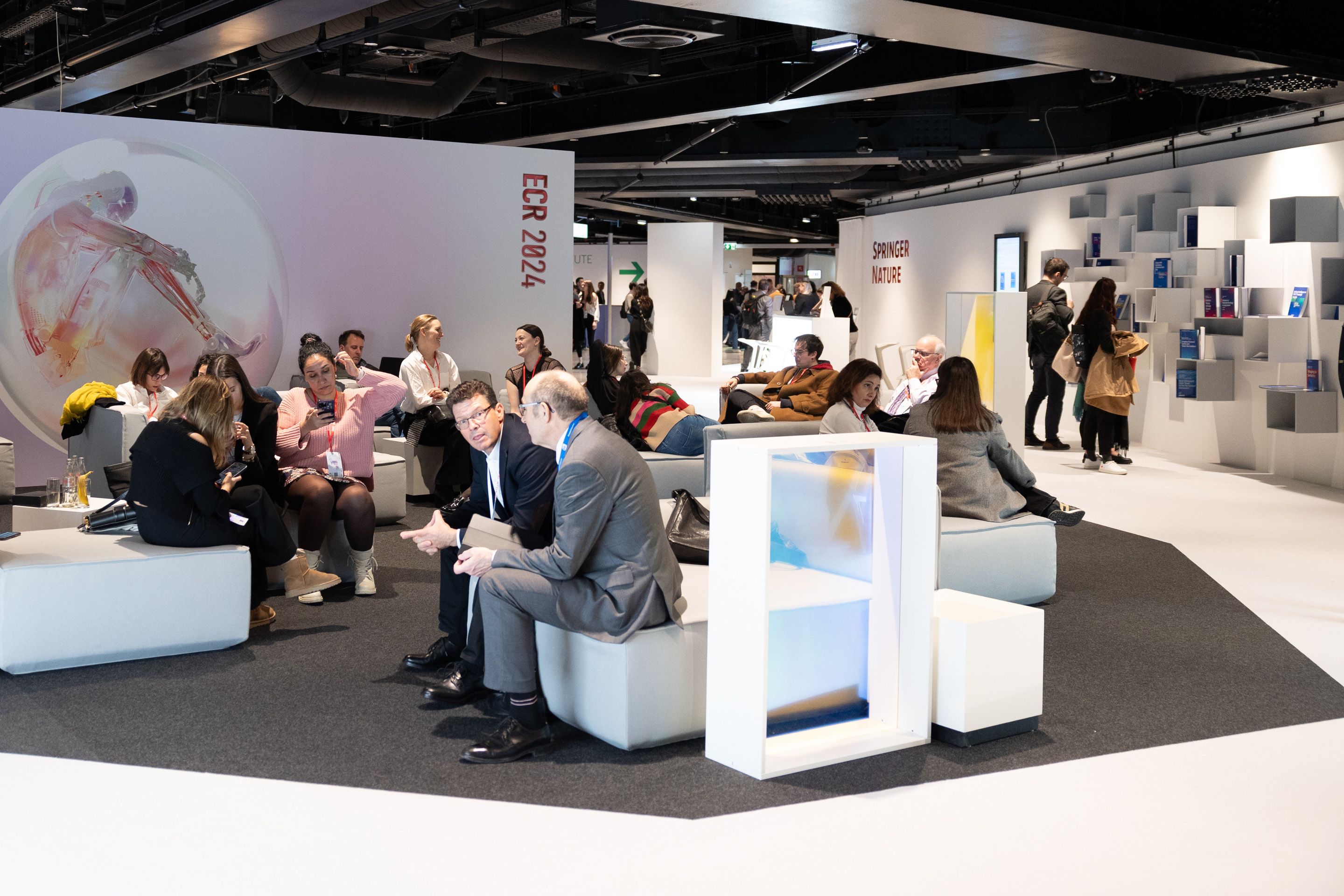 Raum mit weissen Trennwaenden, Sitzcouches und vielen Menschen