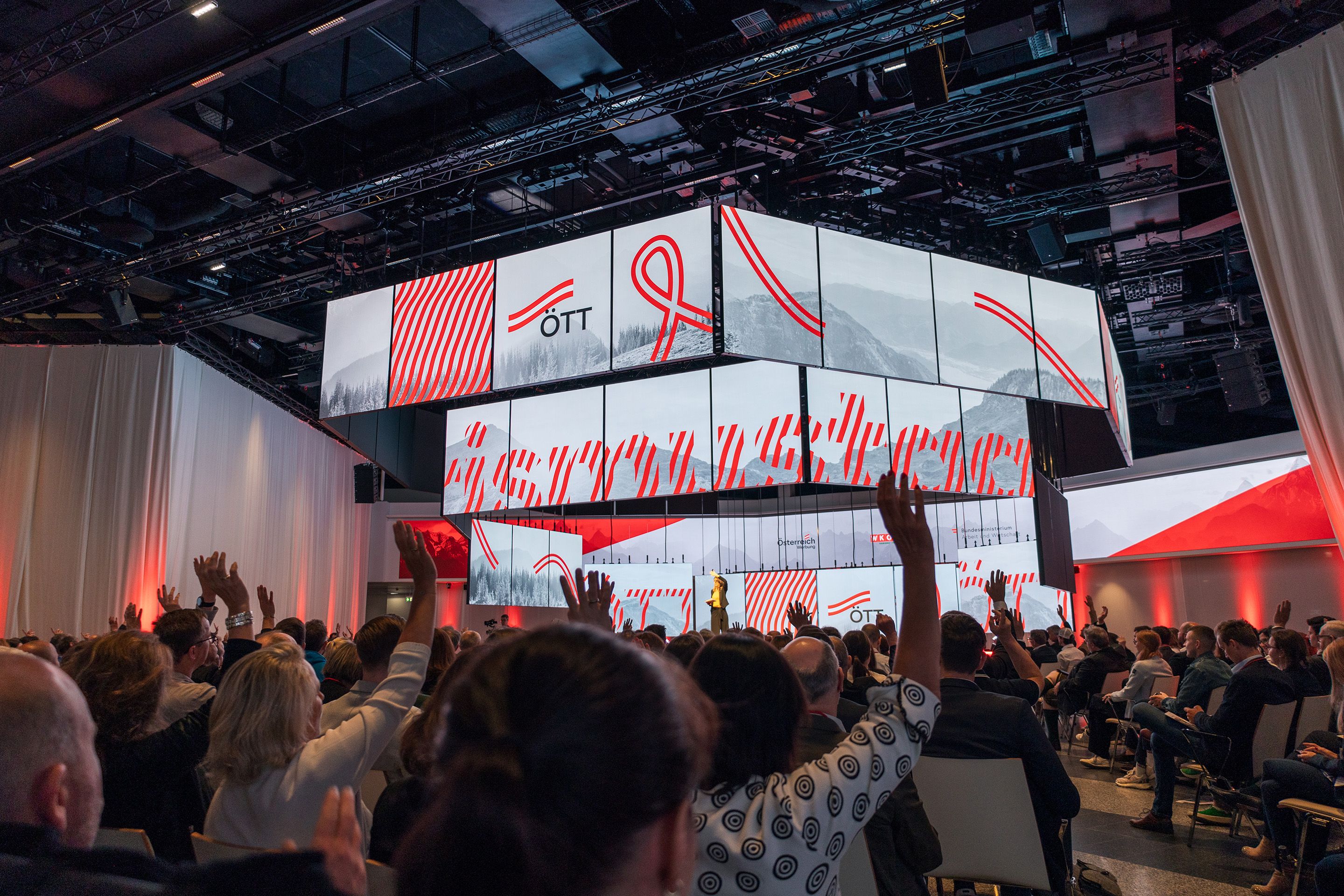 In einem Publikum heben viele Menschen ihre Haende vor der polySTAGE Buehne im Austria Center Vienna.