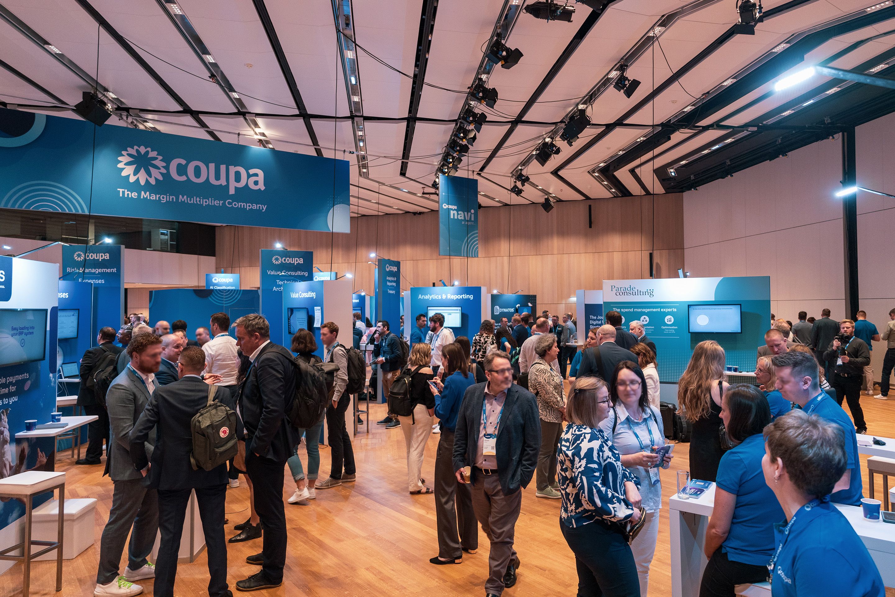 Menschen stehen bei blauen Messestaenden bei einem Corporate Event im Austria Center Vienna.