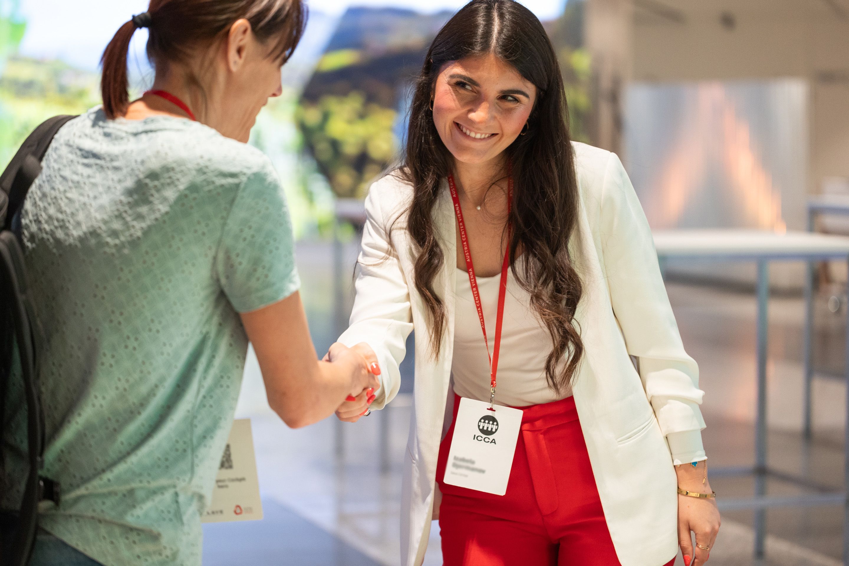 Laechelnde Frau gibt einer anderen Frau die Hand, beide tragen einen Badge fuer ein Event.