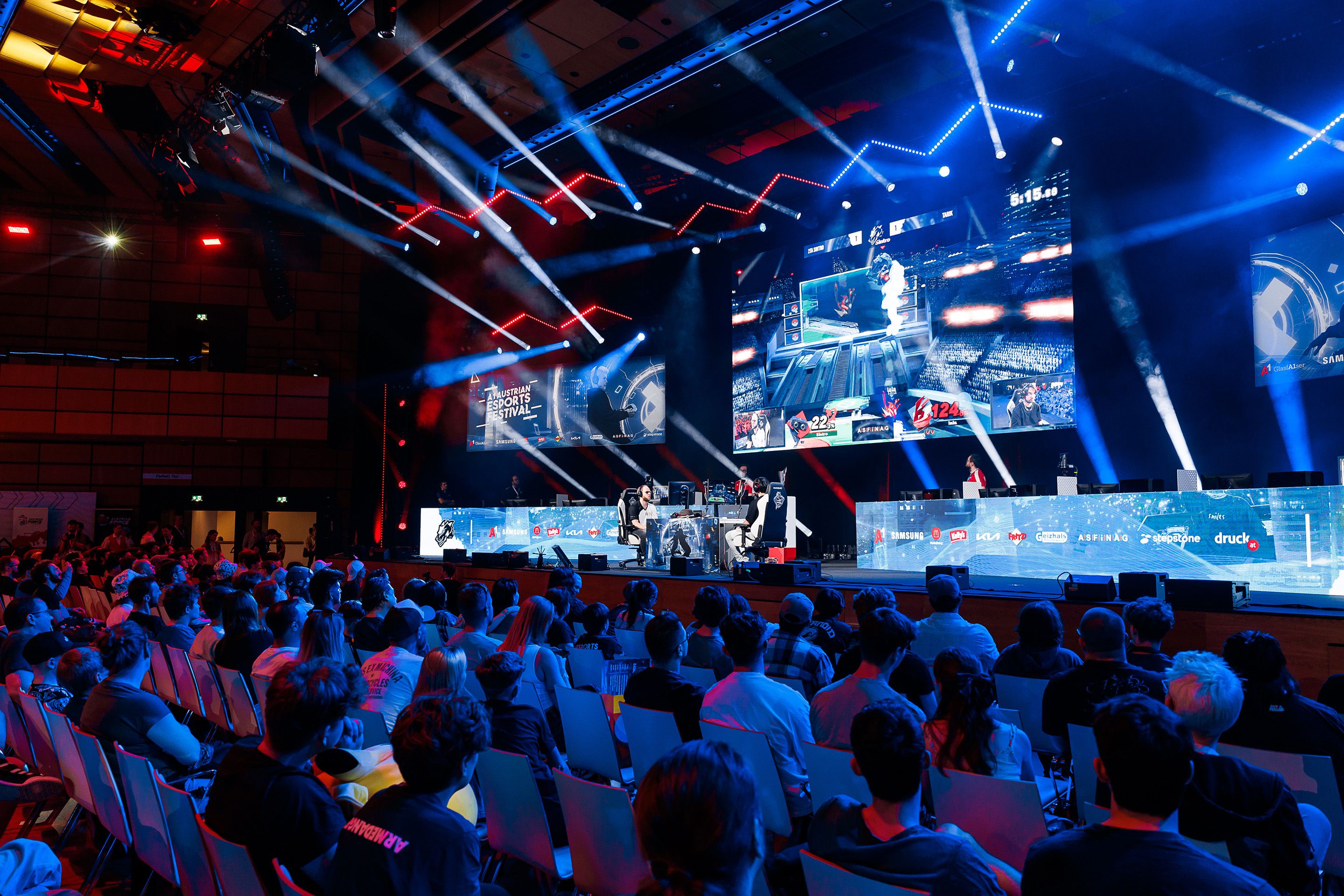 Zwei maennliche Spieler sitzen sich gegenueber und spielen vor Publikum am A1 E-Sports Festival 2024 im Austria Center Vienna.