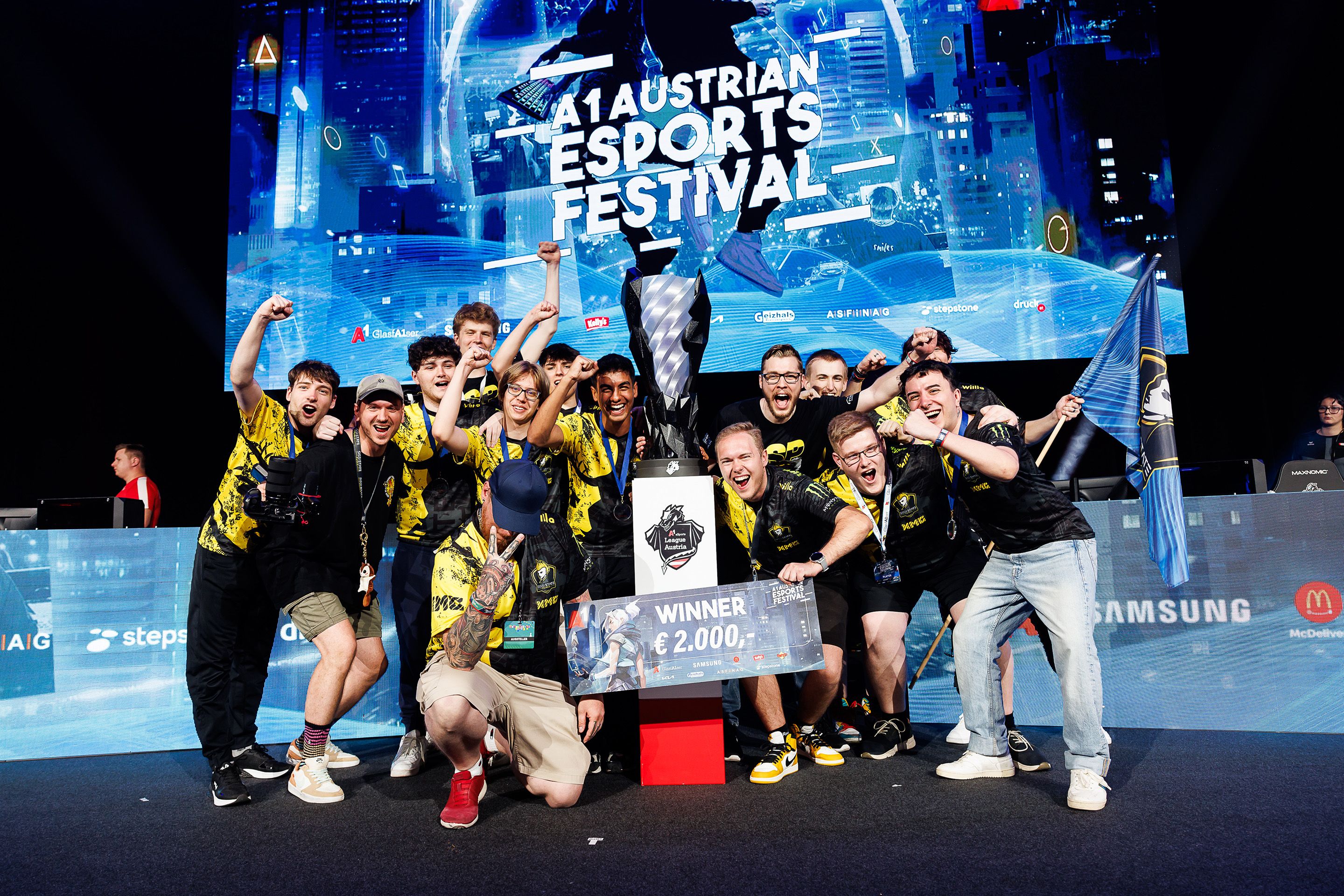 Gruppe schreiender und lachender junger Maenner posieren bei einem Pokal am A1 E-Sport Festival 2024.
