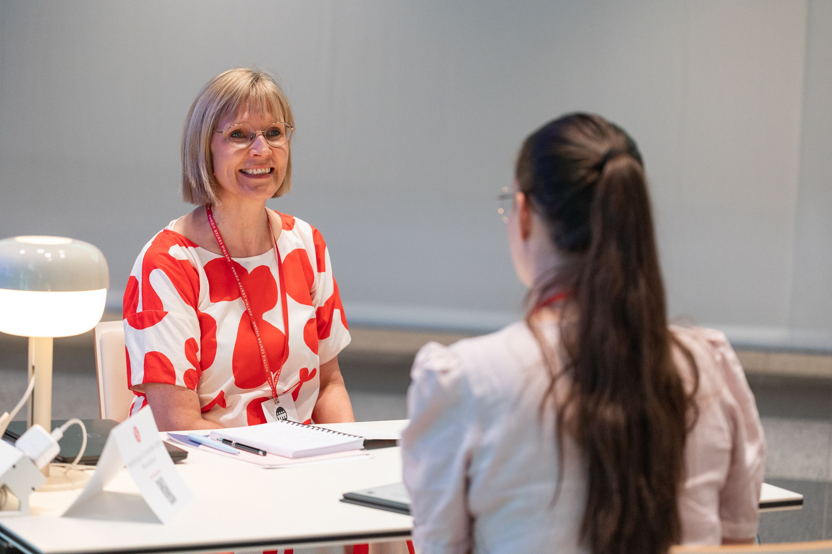 Zwei Frauen an einem Tisch beim Gespraech mit Schreibunterlagen.
