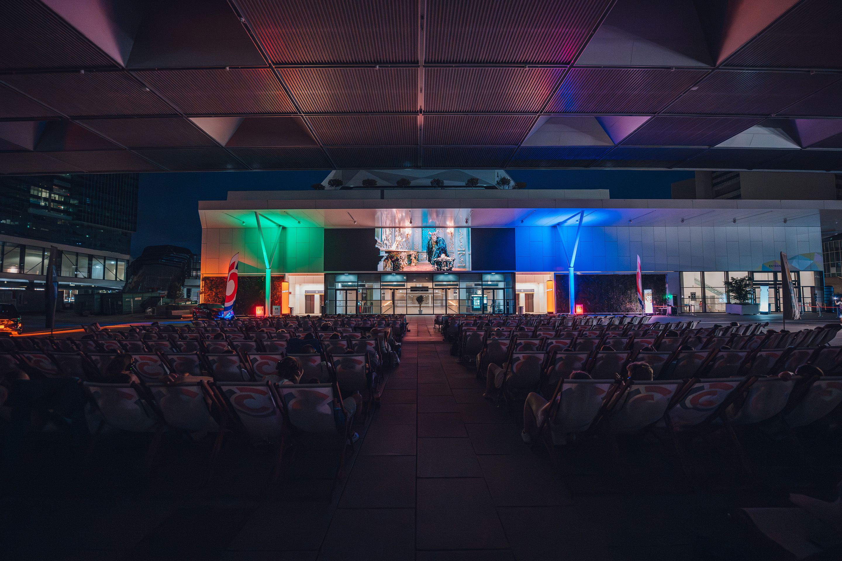 Viele Menschen in Klappsesseln unter dem Dach der Halle X5 Donausegel schauen vor dem Austria Center Vienna beim Silent Cinema einen Film.