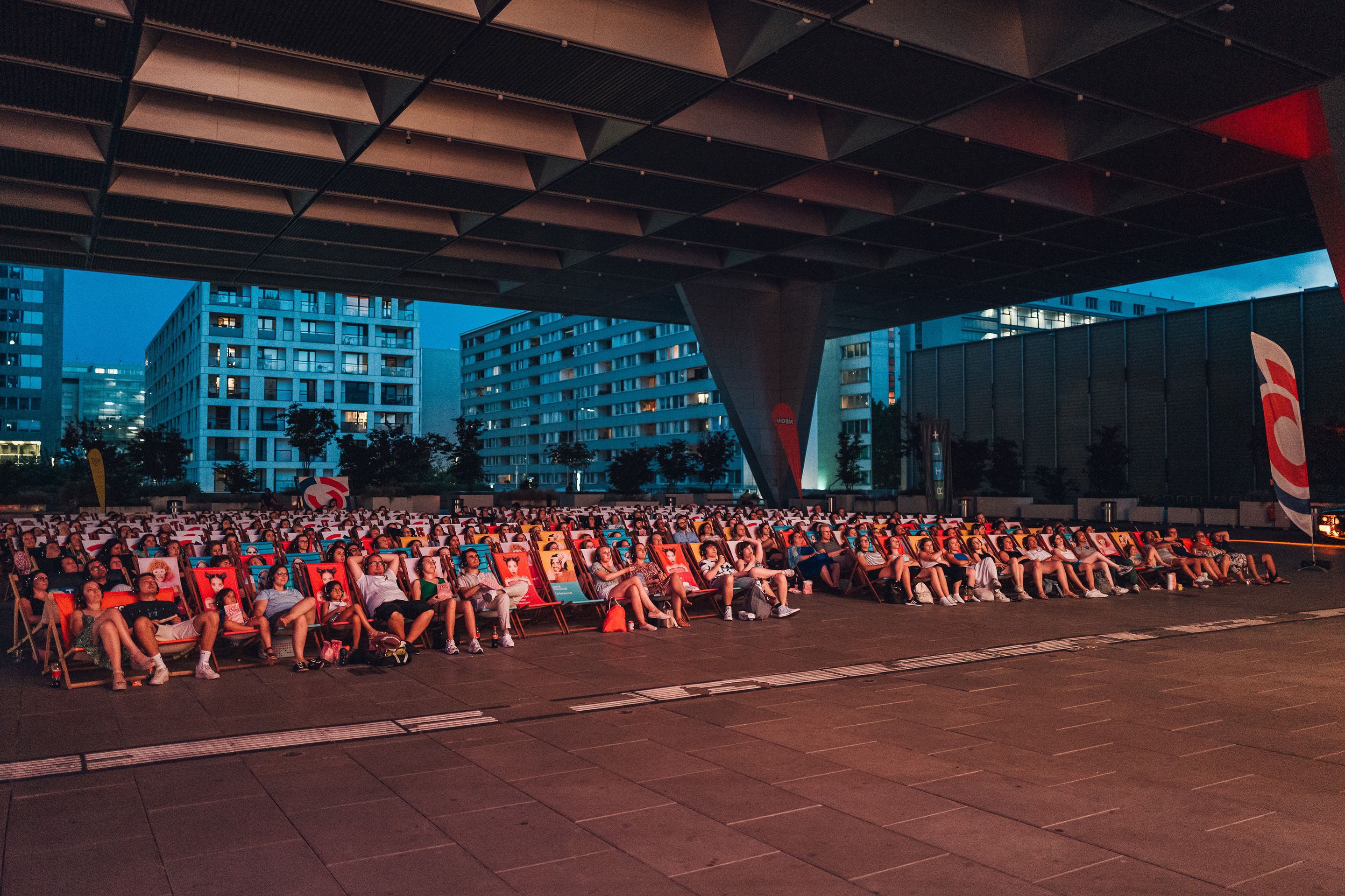 Viele Menschen in Klappsesseln unter dem Dach der Halle X5 Donausegel vor dem Austria Center Vienna beim Silent Cinema.