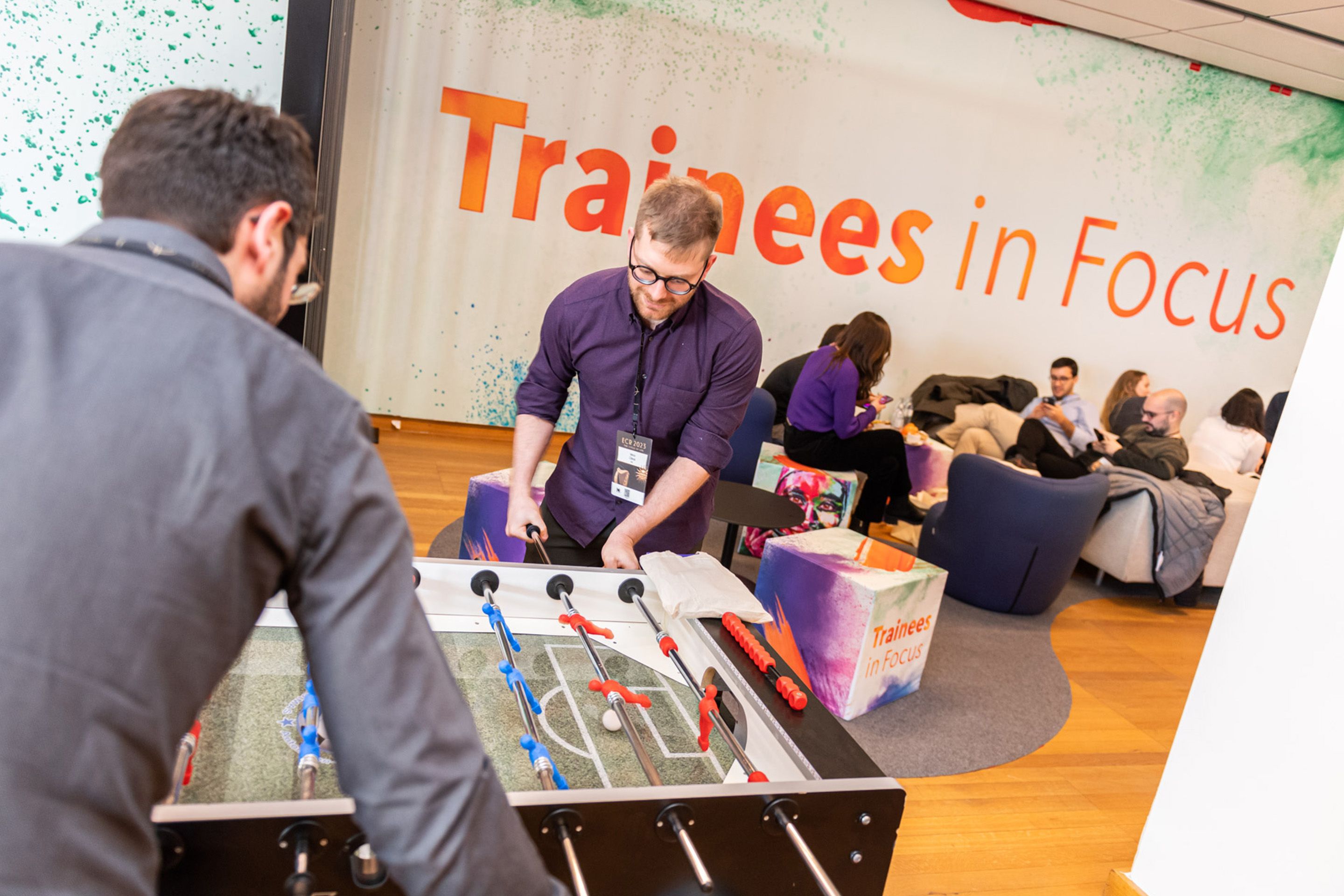 Zwei Maenner spielen Wuzzler Tischfussball, im Hintergrund einige Menschen in Loungesesseln am ECR 2023.