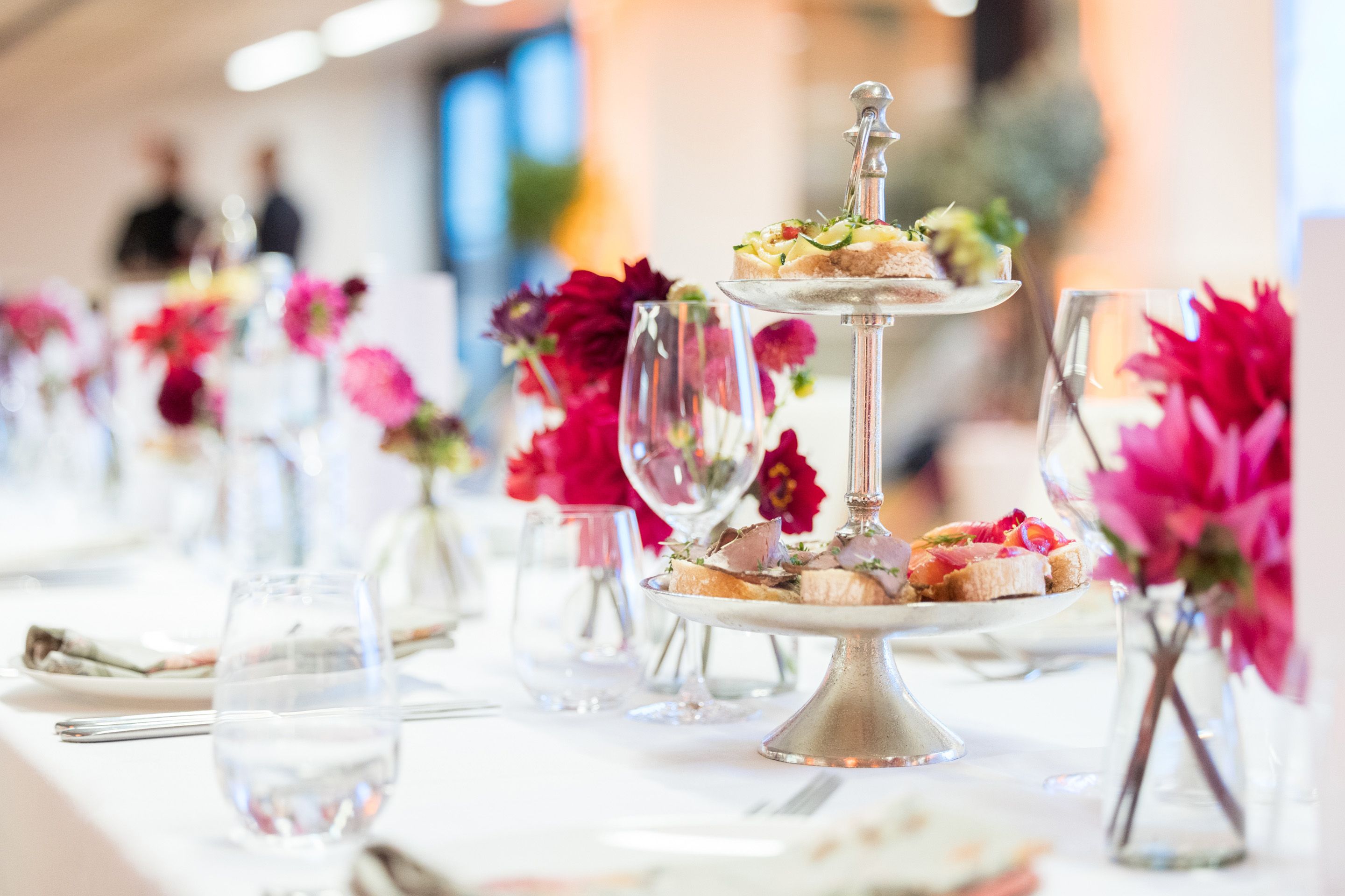 Gedeckter weisser Tisch mit Glaesern, einer Etagere und roten Blumen