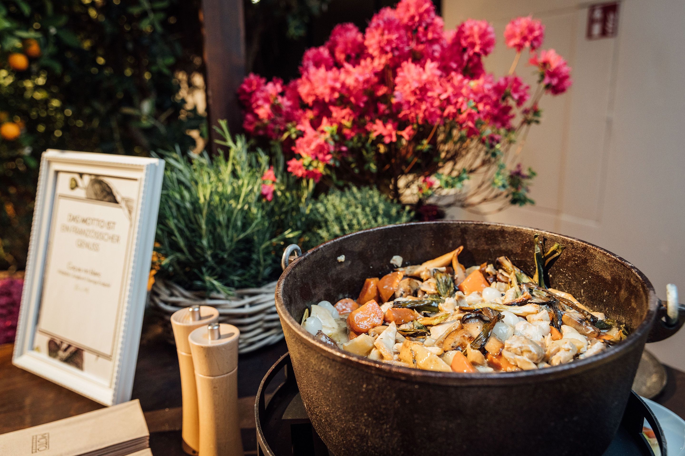 Topf mit Eintopf bei einem Buffet mit Pflanzen und Blumen im Hintergrund