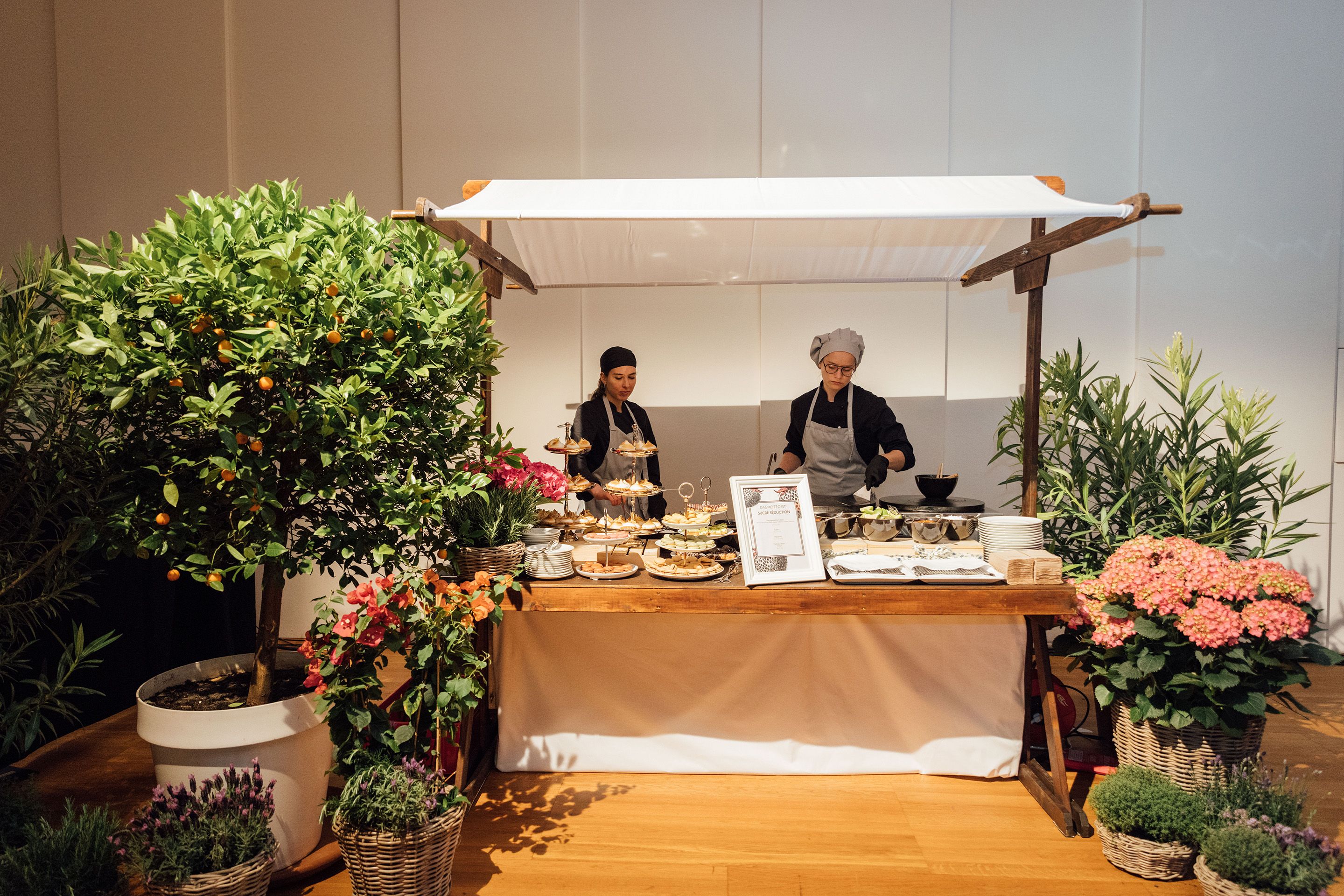 Zwei Frauen stehen an einem Marktstand mit Essen umringt von Blumentoepfen in einem Raum im Austria Center Vienna