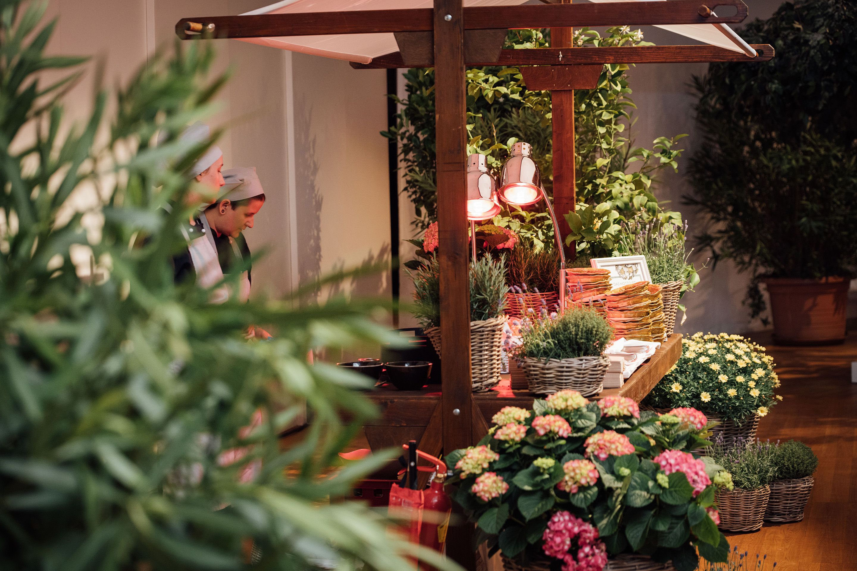 Stand mit Catering und vielen Blumentoepfen und Straeuchern in einem Raum