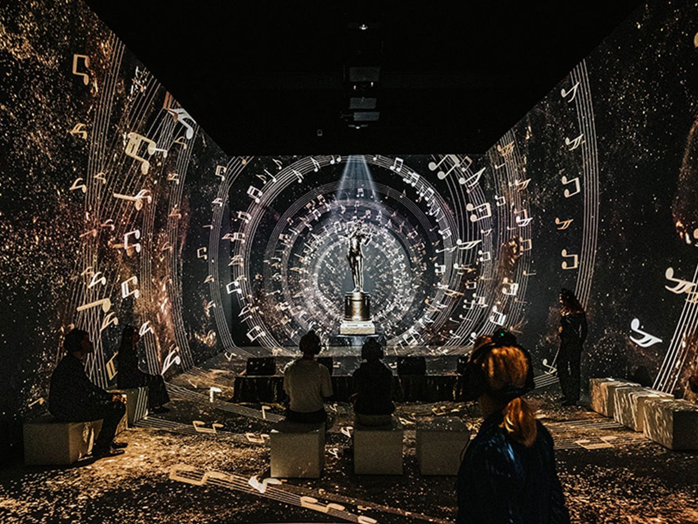 Dunkler Raum mit Lichtprojektionen und einigen Menschen im Johann Strauss Museum