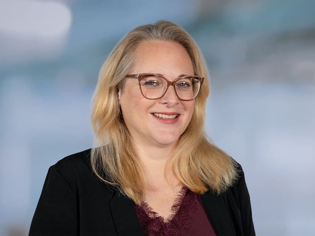 Porträt einer lächelnden Frau mit Brille vor hellem Hintergrund