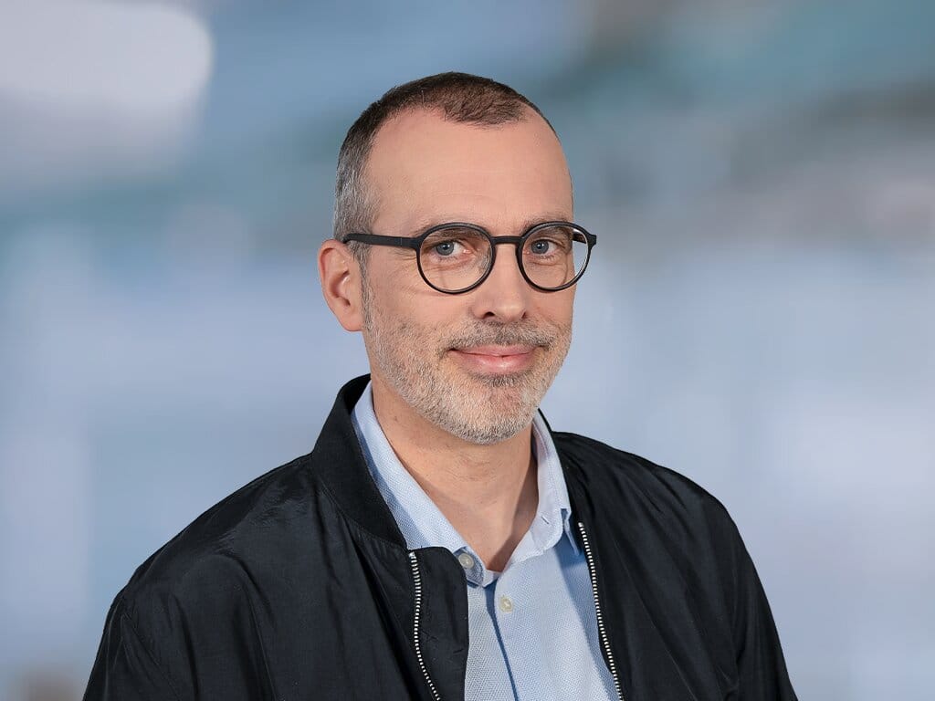 Porträt eines Mannes mit Brille und Bart vor hellem Hintergrund