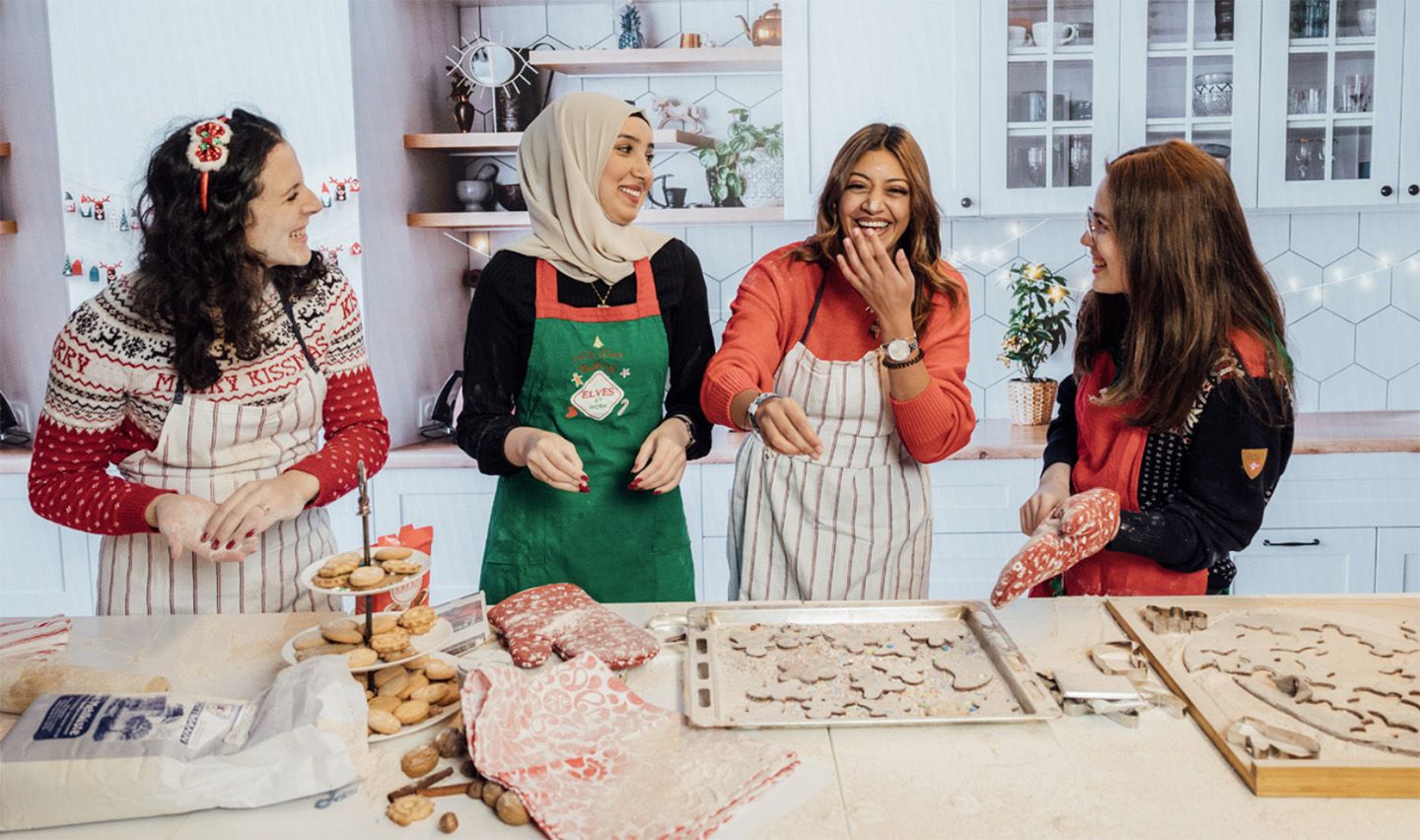 Vier Frauen lachen beim Plätzchenbacken in einer Küche.