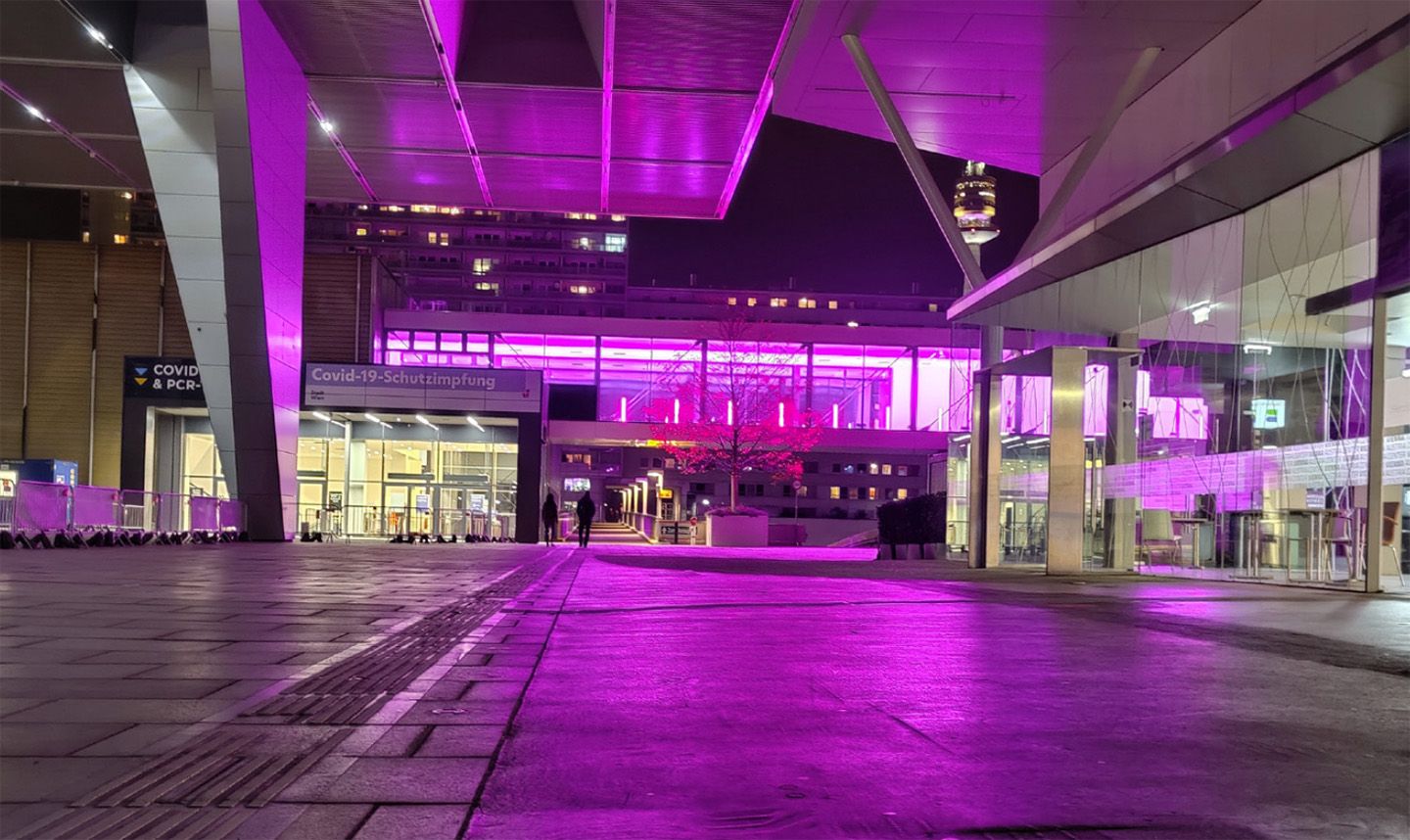Modernes Gebäude bei Nacht, violett beleuchtet, großer Platz.