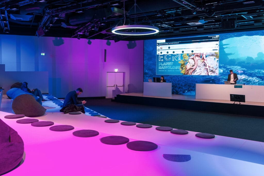 Vortrags-Saal mit farbiger Beleuchtung und einer großen LED-Wand über der Bühne
