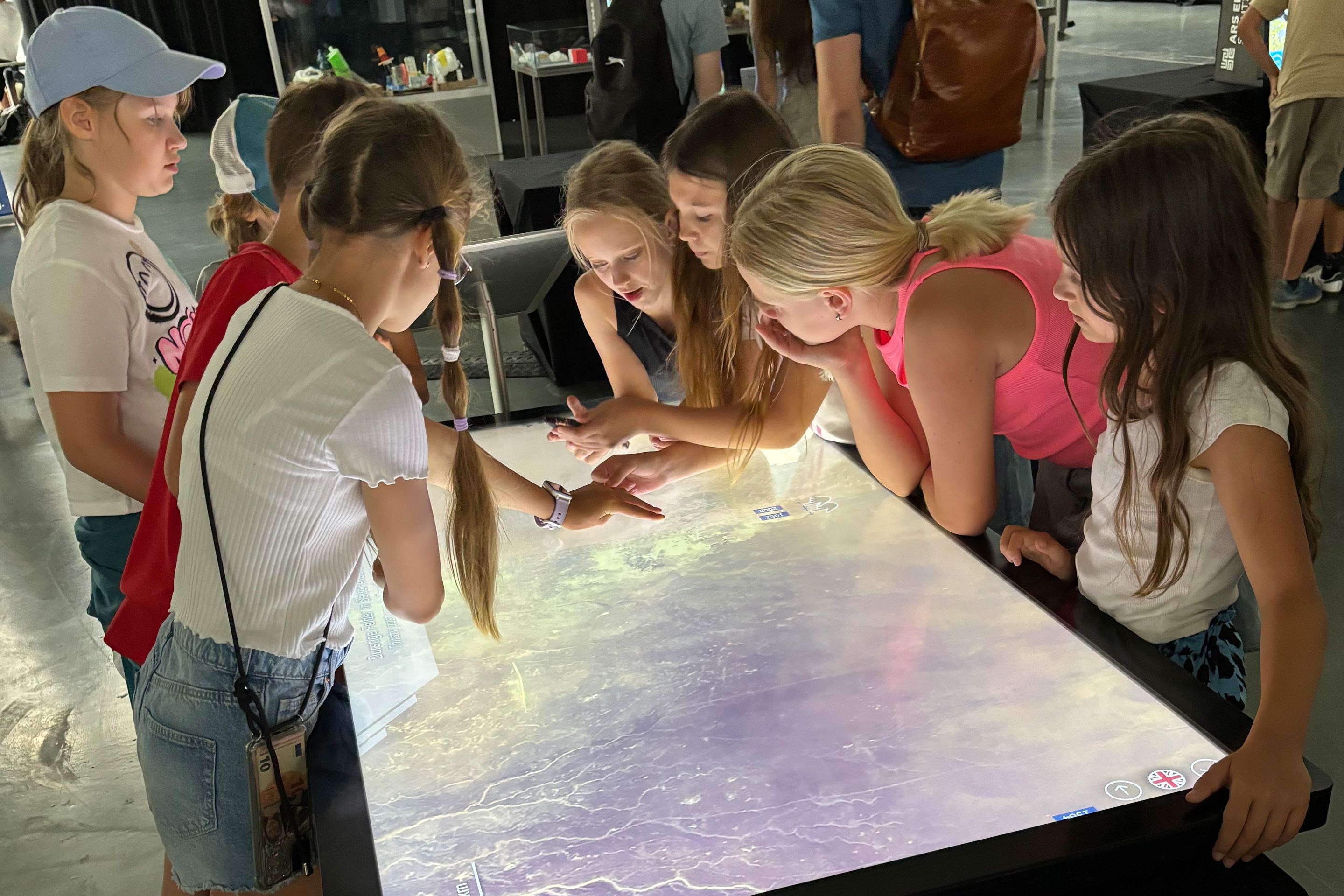 Kinder, die um einen Touchscreen-Tisch stehen und fasziniert forschen